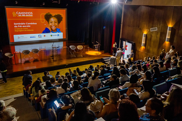 Plateia de gestores e professores da rede de Educação Infantil de Guarulhos Alt Text: Auditório lotado durante o seminário Caminhos da Pré-Escola, com grande tela projetada mostrando o tema do evento.